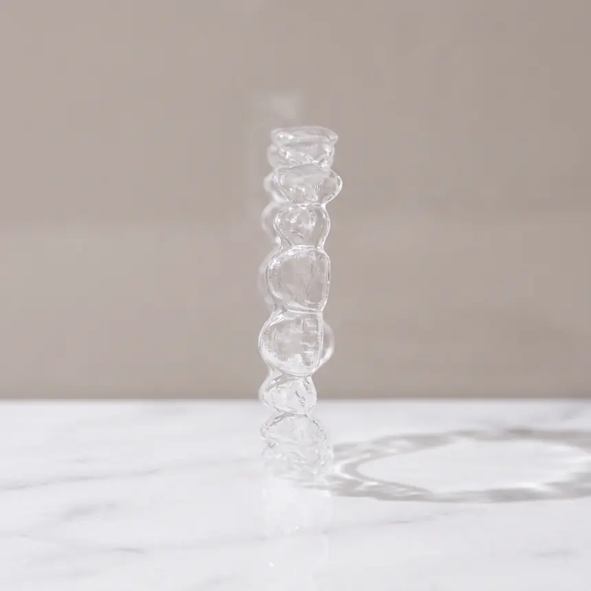 A single clear thermoformed aligner tray standing on honed white marble
